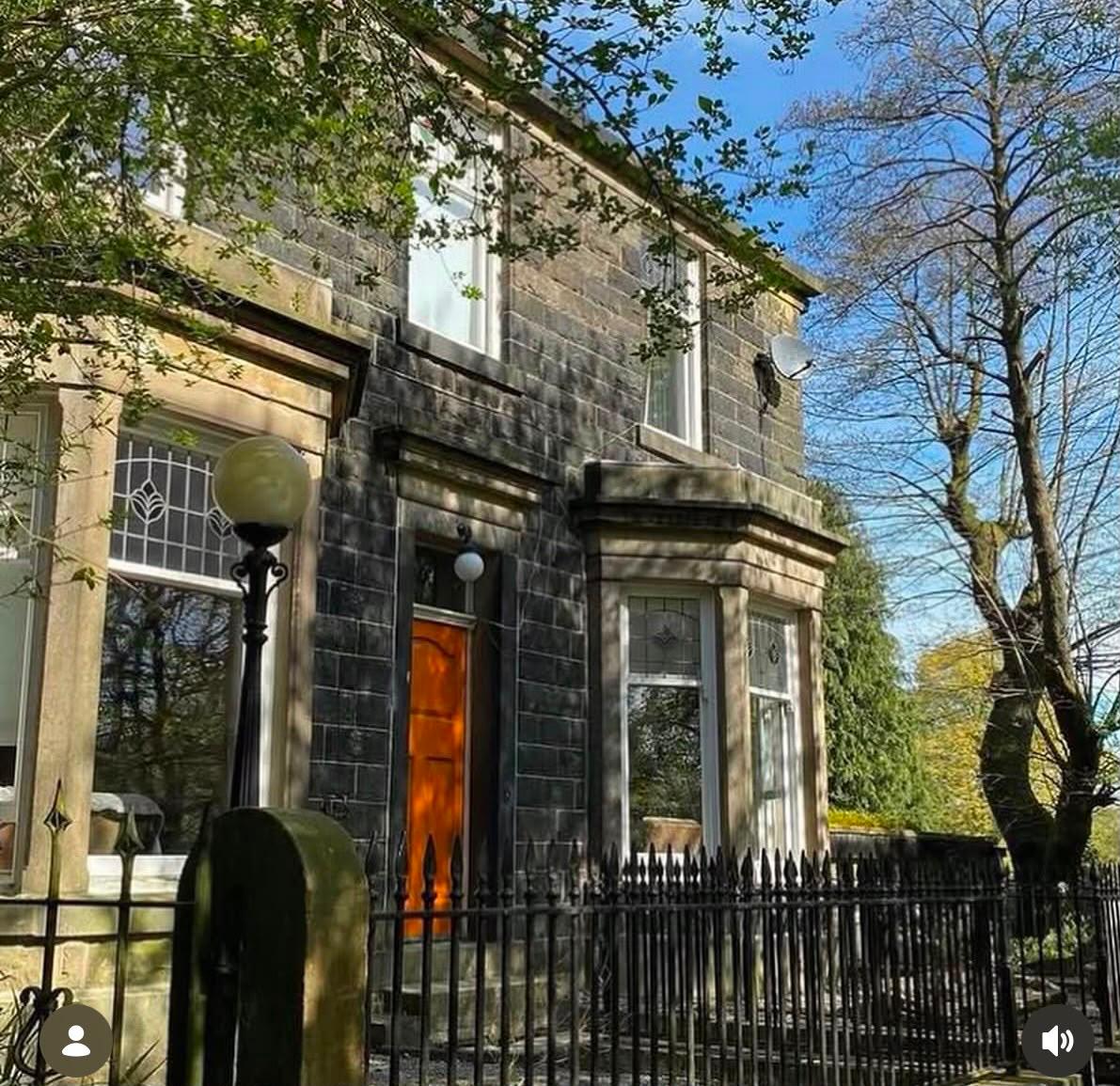 Front elevation of the stone house behind iron railings in spring sunshine