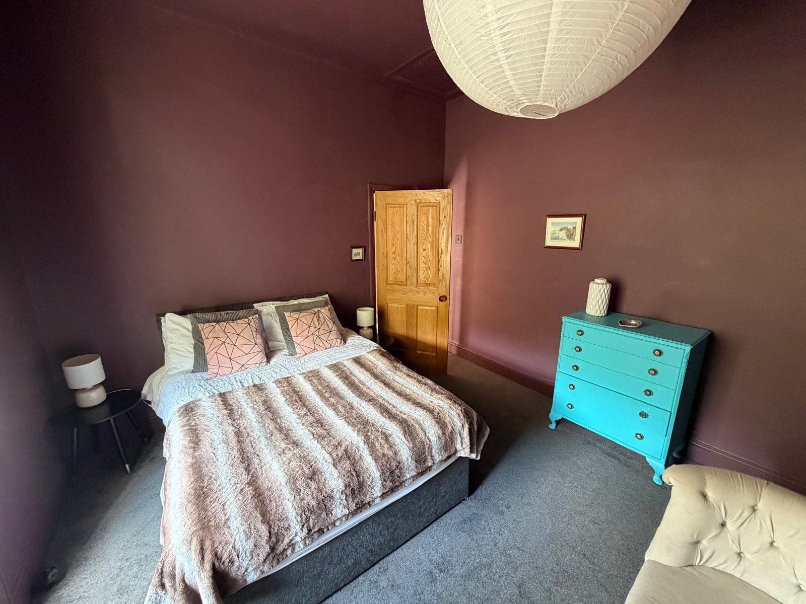 Bedroom with aubergine walls, a striped throw and a turquoise chest of drawers