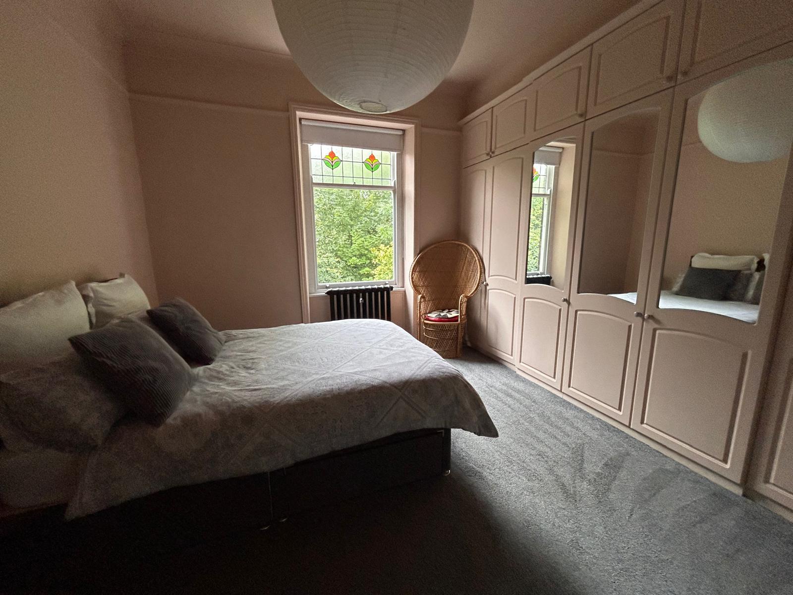 Bedroom with floor-to-ceiling fitted wardrobes, a peacock chair and garden views
