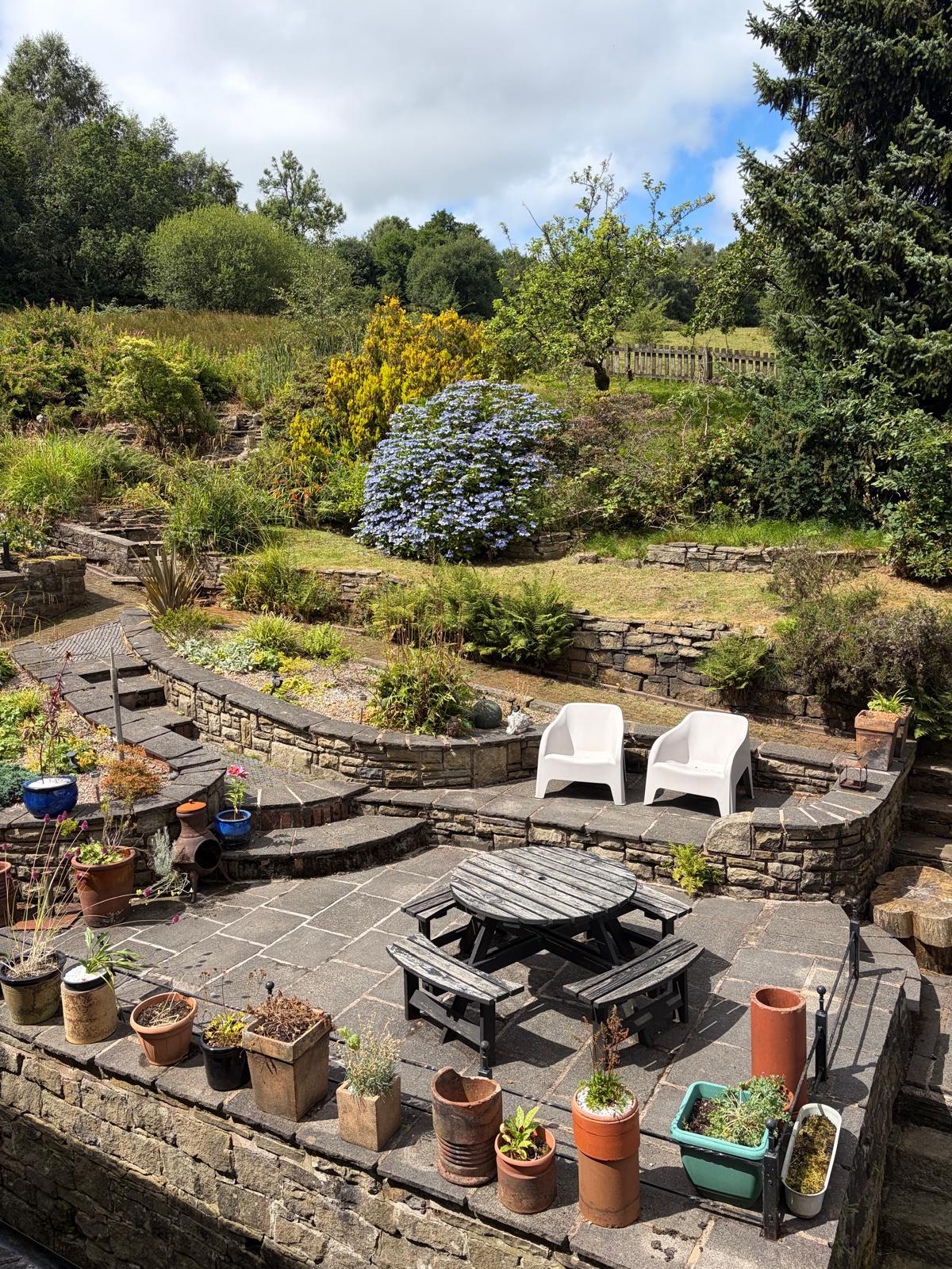 Sunny stone terrace with a picnic table, potted plants and valley views